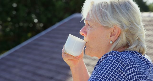Senior Caucasian woman enjoys a cup of coffee outdoors, with copy space. Her serene expression suggests a peaceful morning ritual at home.