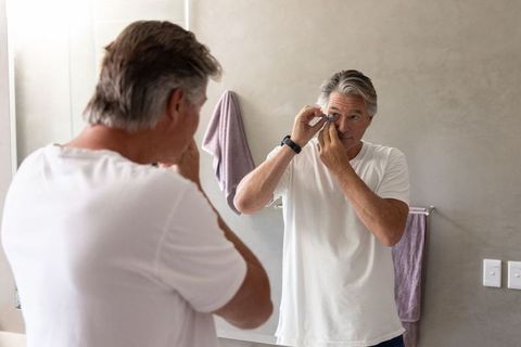 Senior man adjusting contact lens in bathroom mirror during morning grooming routine