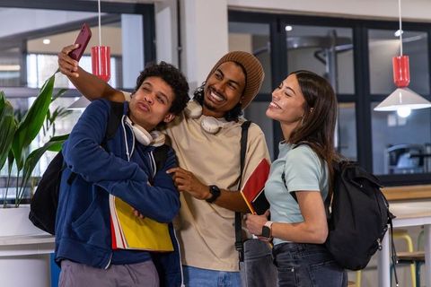 Diverse college students posing for selfie in modern campus lounge holding notebooks