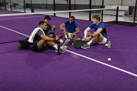 Four male athletes resting on purple indoor pickleball court holding paddles