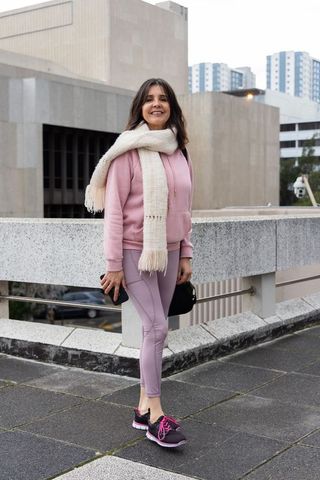 Smiling woman wearing pink hoodie and leggings with cream scarf on urban rooftop terrace
