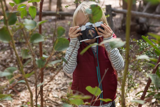 Little girl taking photos in a forest, perfect for themes of childhood exploration, nature activities, and learning photography. Ideal for educational content, nature blogs, and family adventure promotions.