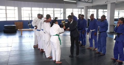Girl receiving trophy in martial arts uniform at gym ceremony