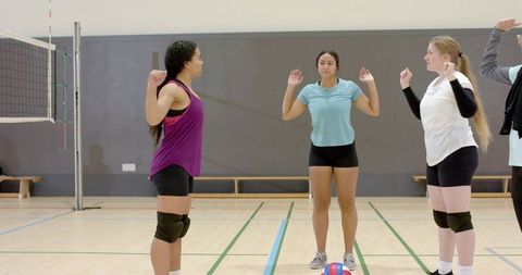 Female volleyball players practicing serve-receive drill on indoor hardwood court with net