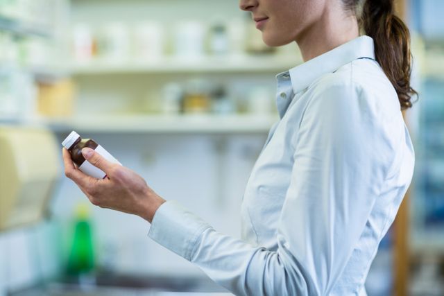 Pharmacist holding and examining a prescription bottle, focusing on accuracy and patient safety in a pharmacy environment. Ideal for illustrating healthcare, pharmaceutical, and medical professions, as well as drugstore operations and prescription filling processes.