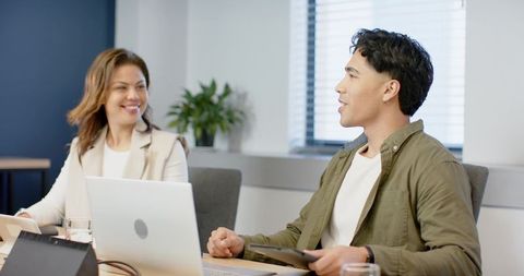 Two colleagues collaborating in meeting room with laptops and tablet for office teamwork