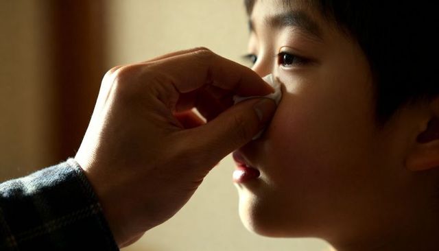 Tender parent wiping child's nose with tissue closeup warm home gentle caregiving moment