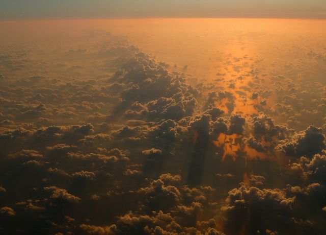 Stunning aerial view of sunset sky with golden hues illuminating the clouds and creating dramatic light rays. Perfect for use in travel promotions, nature documentaries, backgrounds for websites, and inspirational posters.