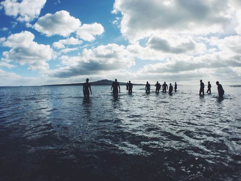 Group of People Walking Through Shallow Ocean Against Vibrant Sky