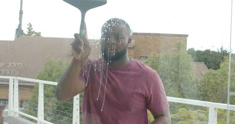 African man cleaning balcony glass with squeegee, outdoor terrace and window care