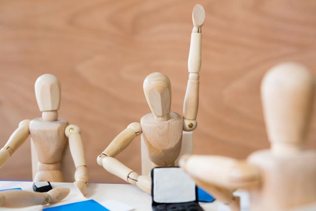Wooden figurine raising hand during a business meeting in a conference room. Ideal for illustrating concepts of teamwork, collaboration, and active participation in professional settings. Useful for business presentations, corporate training materials, and articles on effective communication and leadership.