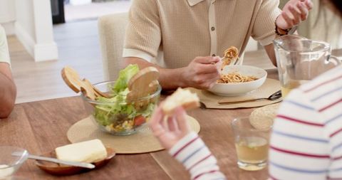 Family enjoying spaghetti meal at wooden dining table