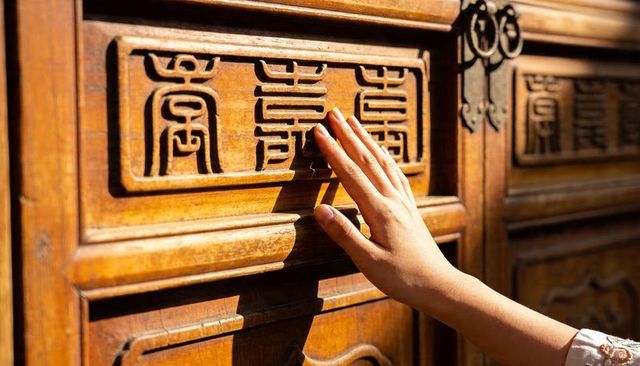 Close-up hand touching ornate carved wooden door panel with metal ring handle in sunlight