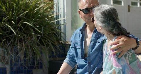 Senior couple sitting on sunlit porch bench sharing tender conversation and embrace
