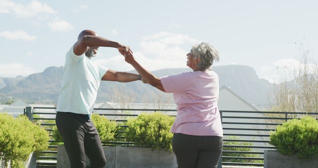 Senior couple dancing outdoors with scenic mountain view in background. Suitable for themes around active aging, senior fitness, retirement, outdoor activities, and the joy of movement. Use for promotional materials, lifestyle blogs, or travel advertisements targeting senior audiences.