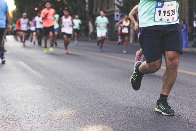 Group of runners participating in a marathon on a city street. The picture captures the determination and athletic spirit of the participants. Use this image for promoting fitness events, sportswear, healthy lifestyle campaigns, and community engagement activities.