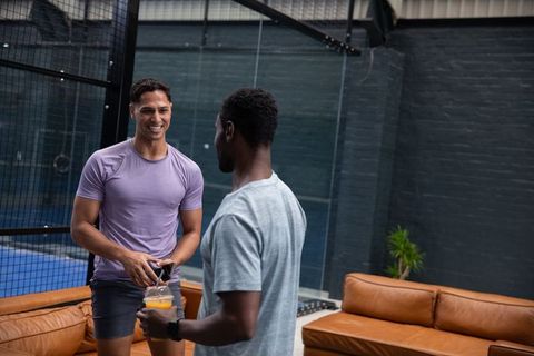 Multiethnic athletes chatting in sports lounge by indoor court holding shaker and phone