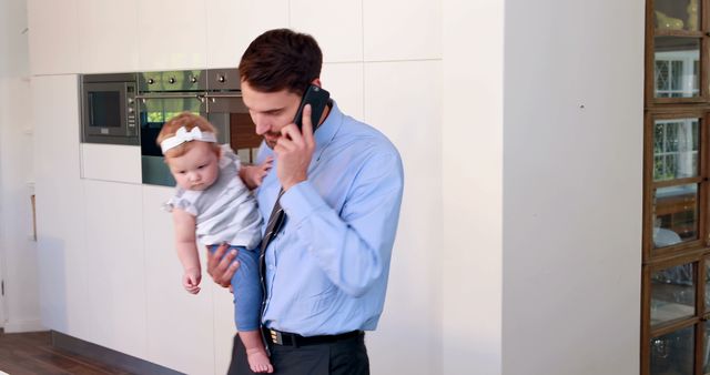 Busy father multitasking while holding baby and talking on phone in modern kitchen - Download Free Stock Images Pikwizard.com