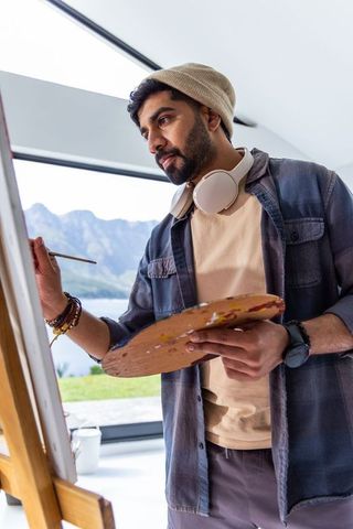 Contemporary artist painting mountain landscape beside panoramic window
