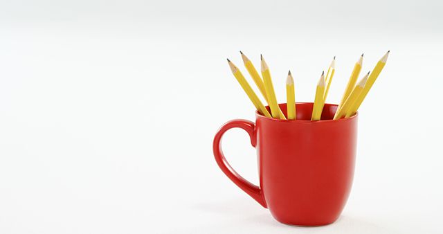 A red mug filled with yellow pencils stands against a white background, with copy space. It symbolizes creativity, the simplicity of design, or the concept of office and school supplies.