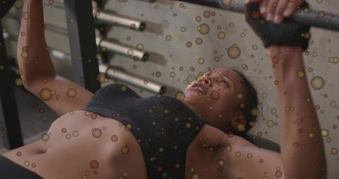 Determined woman pressing dumbbells on bench press during intense gym strength training