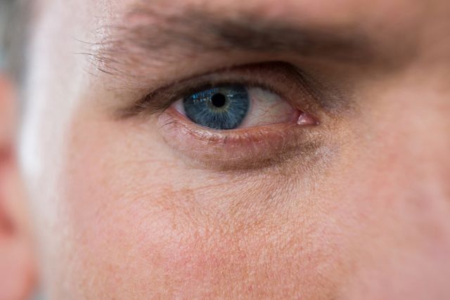 Close-up of a man's blue eye, highlighting the intricate details of the iris and surrounding skin. This image can be used in articles or advertisements related to eye health, vision care, or beauty products. It is also suitable for use in medical or scientific publications focusing on eye anatomy and function.