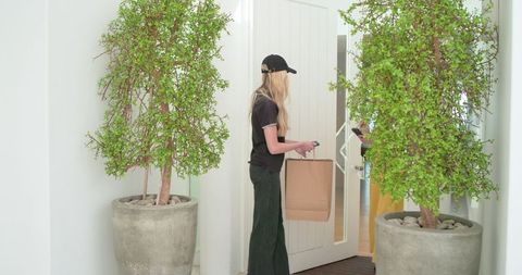 Courier delivering brown bag at residential doorway while scanning handheld device