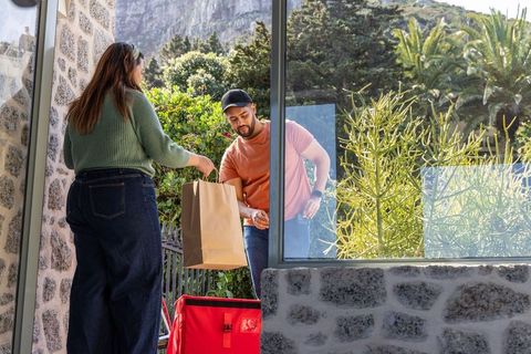 Delivery driver handing grocery bag to customer at porch with red insulated bag