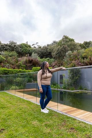 Woman standing beside glass pool railing on wooden boardwalk overlooking reflective pond