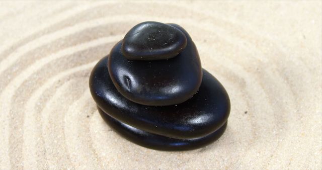 Black stones are stacked in a Zen-like formation on a sandy background with concentric circles, with copy space. This arrangement suggests a peaceful and meditative atmosphere, often associated with relaxation and mindfulness practices.