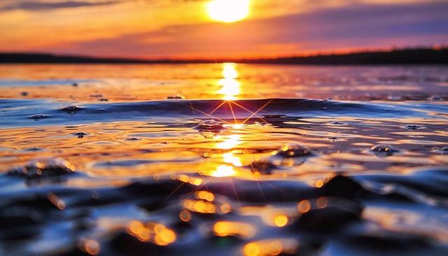 Sunset reflecting on shallow shoreline with starburst droplet, glowing pebbles and ripples