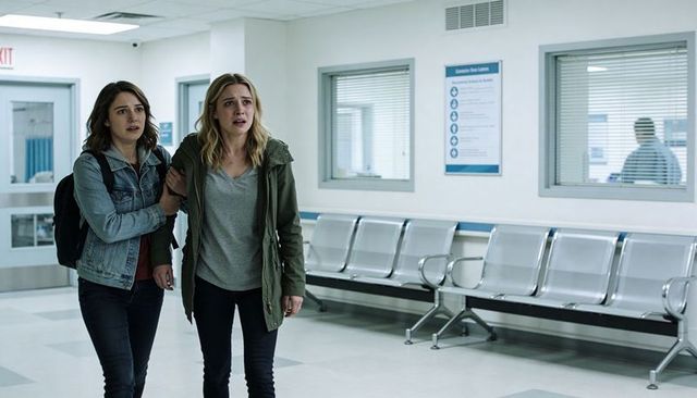 Two women walking through hospital corridor supporting distressed friend during anxious medical visi