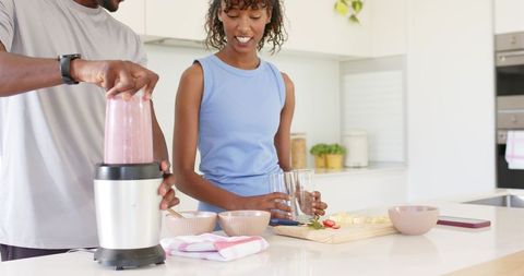 African american couple preparing pink smoothie at bright modern kitchen island