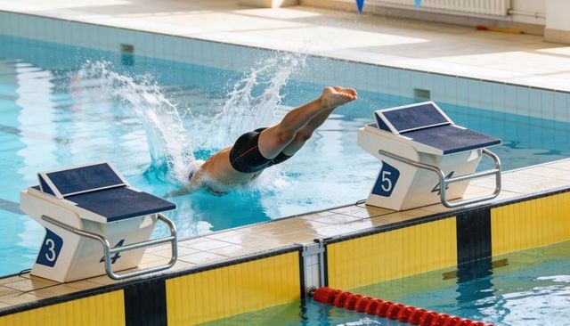 Competitive swimmer diving from starting block into lane splashing water motion and speed