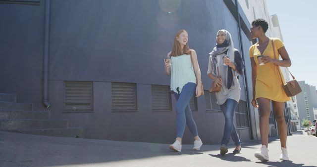 Three diverse young women walking together on a sunny day. They are chatting and smiling, showcasing friendship and unity in an urban environment. Use this for youth lifestyle campaigns, diversity-focused projects, or social group activities.