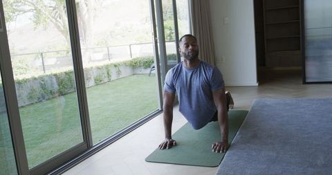 Man practicing upward dog yoga by sliding doors on mat with backyard view, natural light
