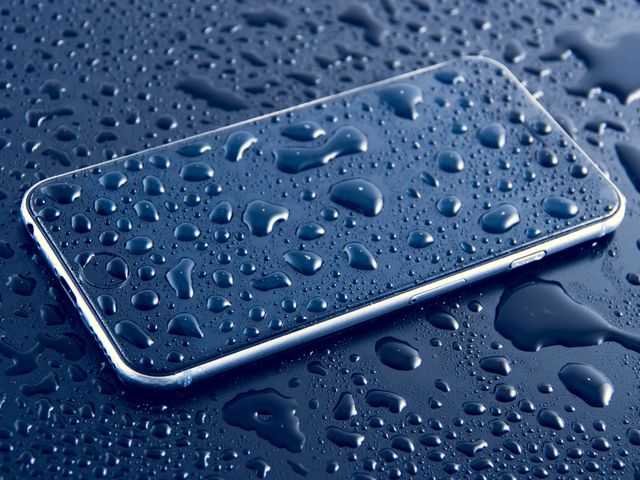 Wet smartphone covered in water drops, emphasizing water-resistant feature. Useful for illustrating smartphone durability, waterproof phone features, electronics reviews, and mobile technology advertisements.