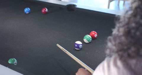 Woman preparing pool shot on black-felt table with cue and colorful billiard balls