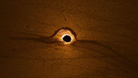 Burned paper puncture with glowing halo macro texture revealing torn fibers and grain