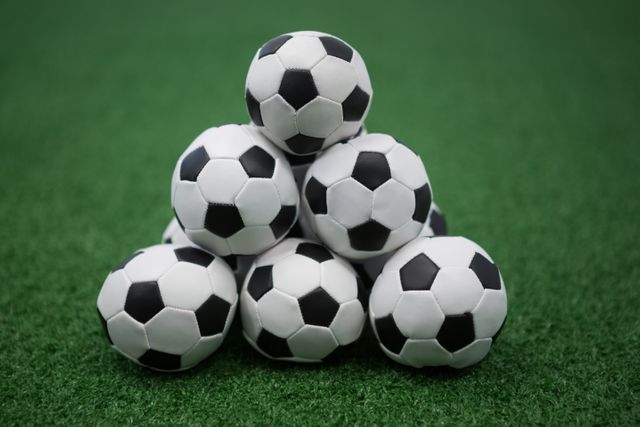 This image shows a stack of soccer balls on artificial grass, ideal for use in sports-related content, advertisements for sports equipment, or promotional materials for soccer events. It can also be used in articles about team sports, recreational activities, or training sessions.