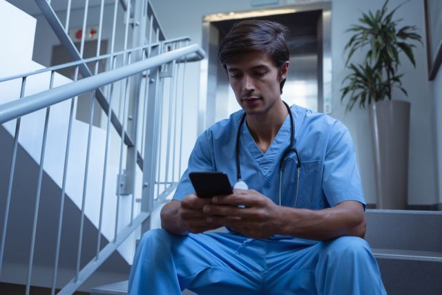Front view of Caucasian male surgeon using mobile phone on stairs at hospital