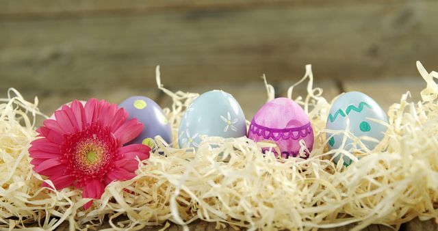 Colorful Easter eggs are nestled in straw with a vibrant pink flower, symbolizing springtime and Easter celebrations. These decorated eggs represent creativity and the joy of the Easter holiday.