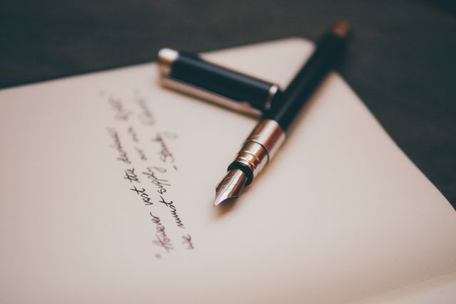 This close-up of a fountain pen lying on an open notebook captures a sense of elegance and professionalism. The handwritten notes on the paper indicate active use, making it ideal for marketing materials related to stationery products, office supplies, or professional writing services. It can also be used in blogs that discuss handwriting, journaling, or the art of letter writing.
