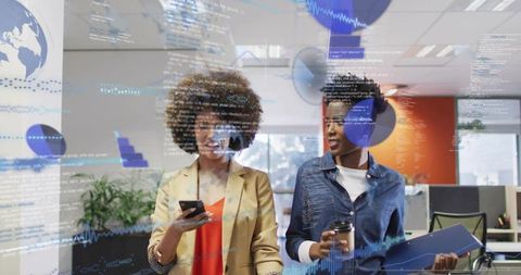 Two women collaborating in modern office walking with coffee phone and digital data overlays