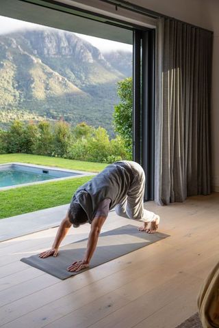Morning yoga stretching on mat by open sliding door with mountain view and pool
