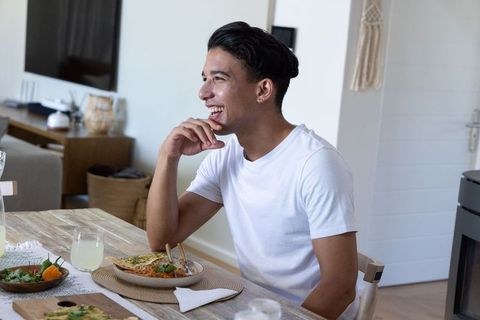 Young man laughing while enjoying relaxed homemade meal at cozy modern wooden dining table