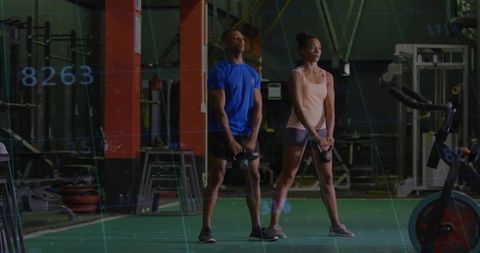 Diverse Duo Engaging in Kettlebell Training on Gym Turf