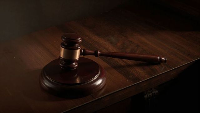 Polished wooden gavel with brass band resting on courtroom bench in dramatic lighting