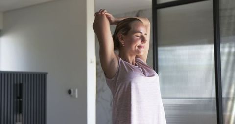 Young woman stretching in minimalist apartment morning calm daylight near frosted glass