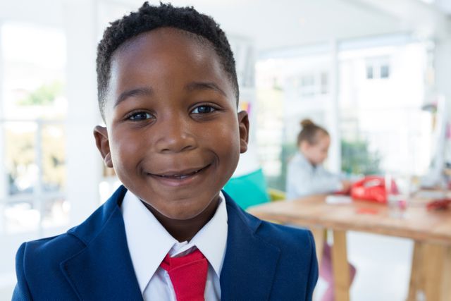 Young boy dressed in a business suit smiling confidently in an office environment. Ideal for use in educational materials, career guidance content, advertisements promoting children's clothing, or articles about future leaders and young professionals.